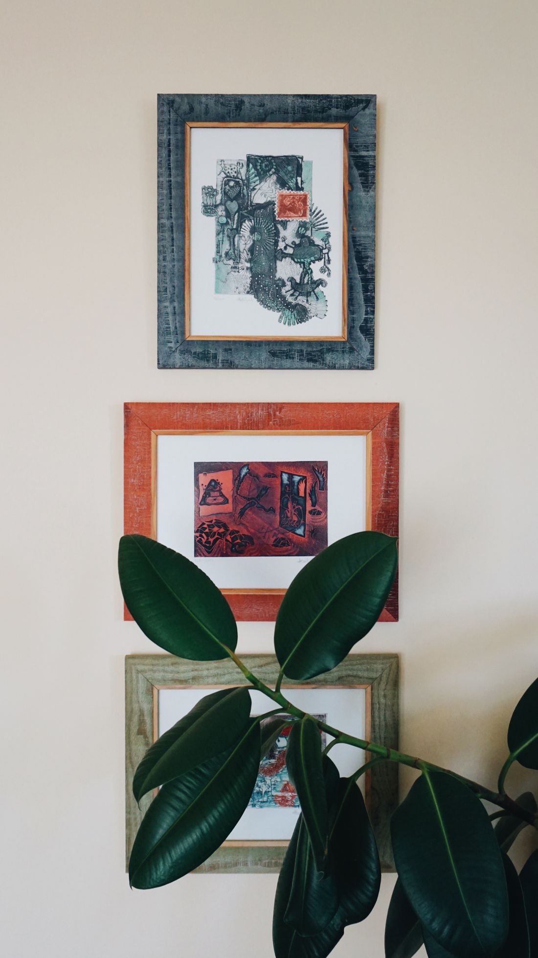 Three varied framed pictures arranged with generous spacing on a plain wall behind a houseplant.