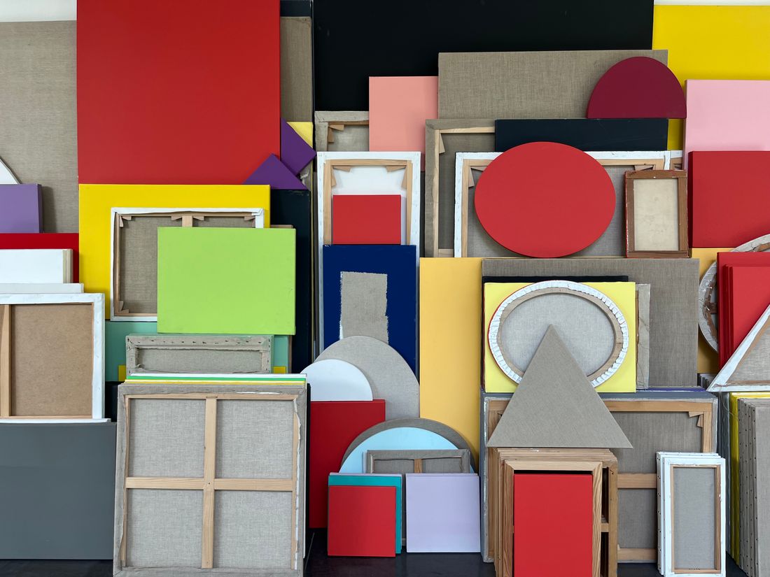 A colorful arrangement of framed and unframed geometric artworks stacked together.